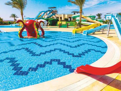 Colorful water playground with slides and palm trees by the pool under blue sky.