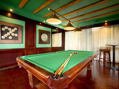 Salle confortable avec table de billard, plafond vert et tabourets près de grandes fenêtres avec rideaux.