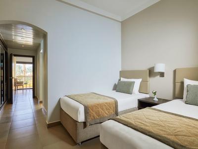 Habitación de hotel con dos camas individuales, paredes blancas y vista a un balcón.