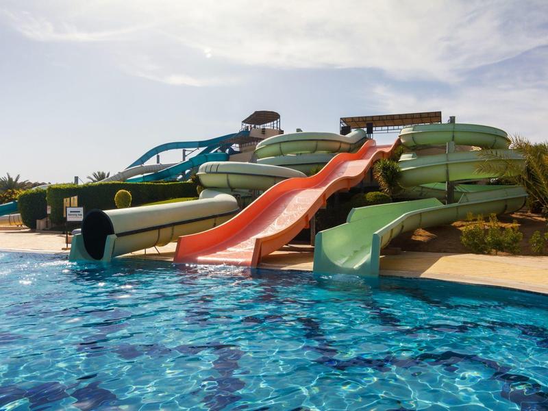 Varias resbaladillas de agua de colores desembocan en una piscina azul bajo el sol.