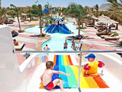 Kinder rutschen auf bunten Wasserrutschen in einem sonnigen Wasserpark mit Palmen.