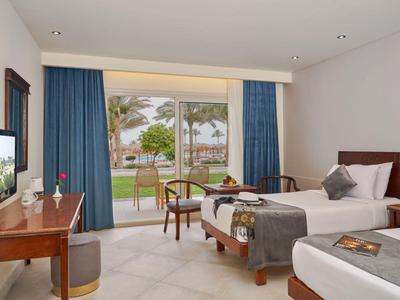 Habitación de hotel con dos camas individuales, escritorio, sillas y vista al jardín y piscina.