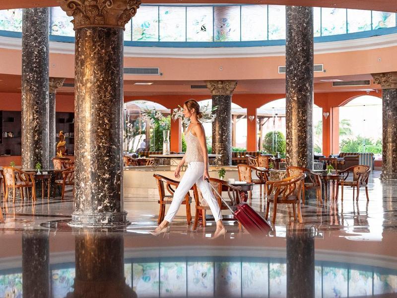 Lobby luminosa de hotel con columnas redondas, áreas de estar y una fuente decorada con cascada.