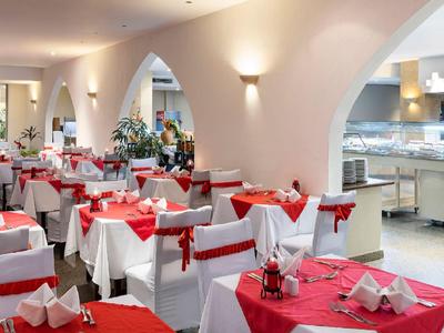 Eleganter Speisesaal mit eingedeckten Tischen in weiß-rotem Farbschema und offenem Buffetbereich