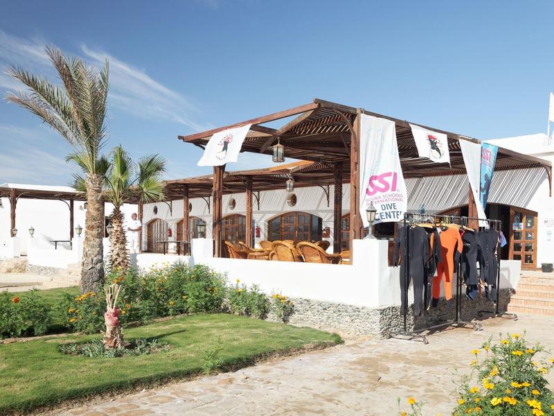 Diving center with wetsuits and shaded sitting area surrounded by palm trees and plants.