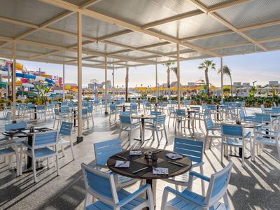 Terrasse de restaurant en plein air avec nombreuses tables et chaises blanches sous un toit léger.