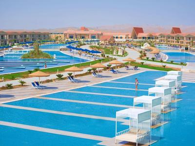 Großer Poolbereich mit einzelnen Tagesbetten in einem Hotelresort unter klarem Himmel.