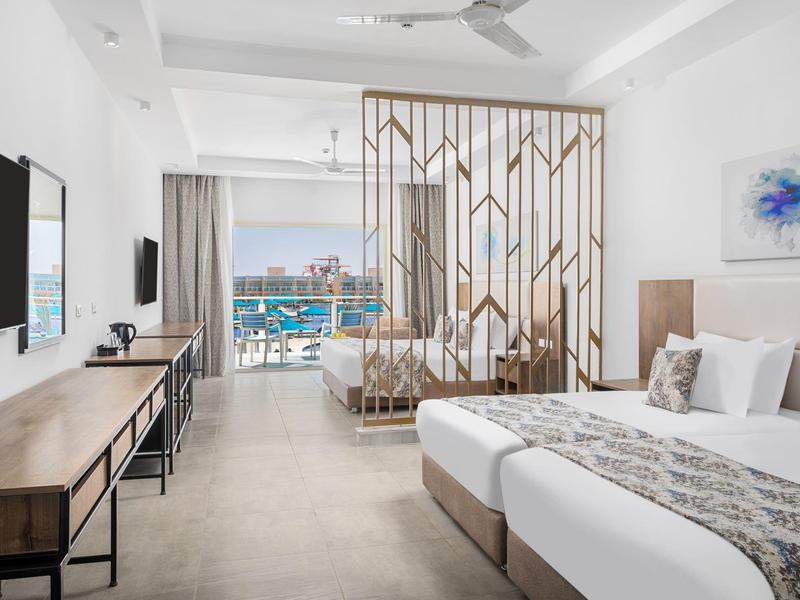 Chambre d'hôtel moderne avec lits jumeaux et vue sur la piscine depuis le balcon.