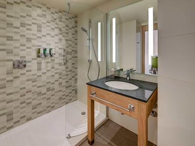 Moderne Hoteldusche mit Holzwaschbecken, großem Spiegel und beleuchteten Spiegelleisten.