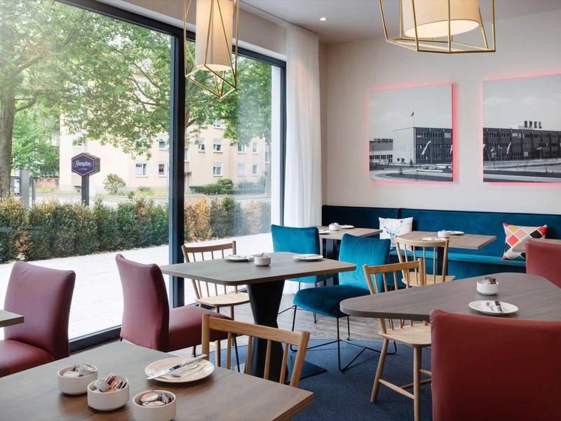 Modernes Café mit roten Sesseln, Holztischen, großen Fenstern und Stadtbild-Gemälden an der Wand.