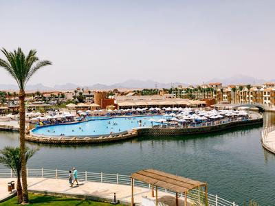 Groot hotelzwembad met parasols, omgeven door water en gebouwen onder een heldere lucht.