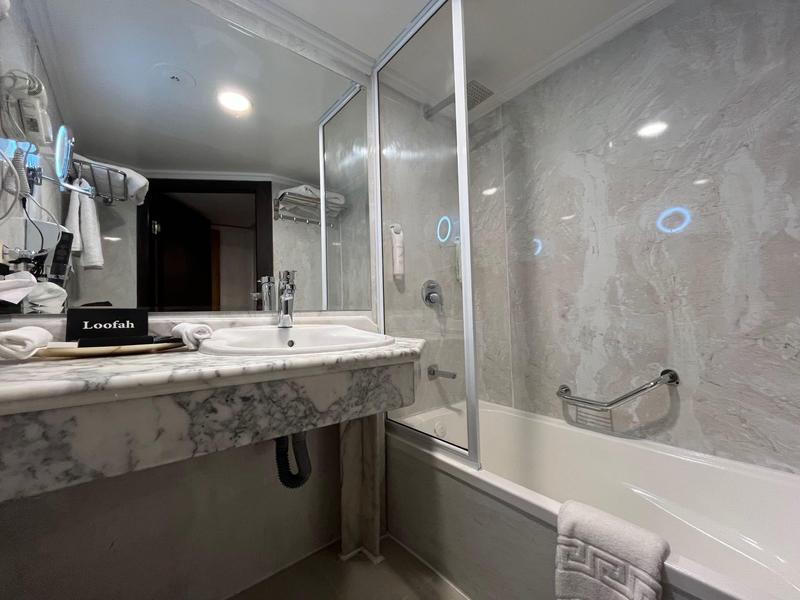 Moderne Badezimmer mit grauen Fliesen, großer Spiegel, Waschbecken, Badewanne und Handtüchern.