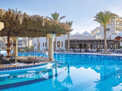 Grande piscine avec bar, palmiers et bâtiment d'hôtel blanc sous un ciel clair