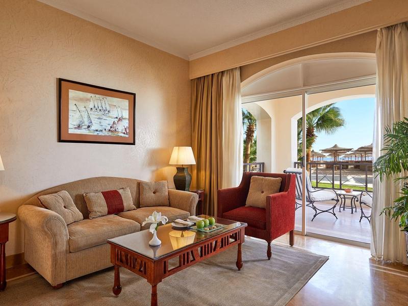 Helles Wohnzimmer mit cremefarbener Couch, rotem Sessel, Holztisch und Zugang zur Terrasse.