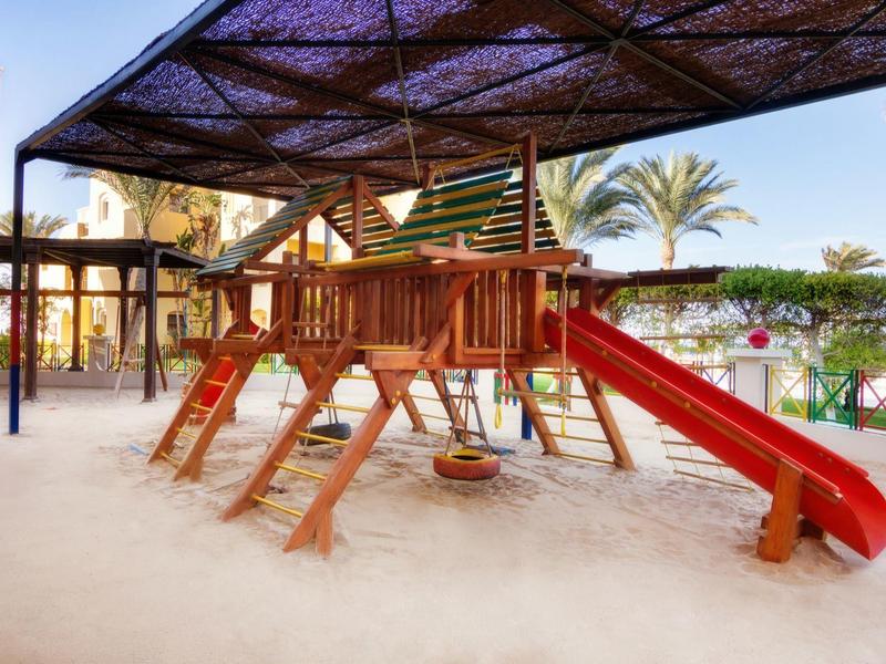 Kinderspielplatz mit Rutsche und Kletternet unter schattenspendendem Dach in einem Hotel.