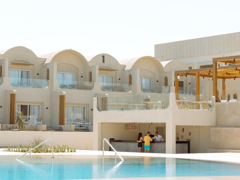 Moderner Hotelkomplex mit Balkonzimmern und großem Schwimmbecken unter blauem Himmel.