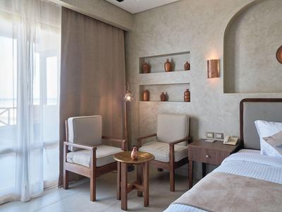 Bright hotel room with balcony, two chairs, small table, and modern decor.