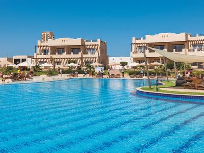 Large blue outdoor pool in front of a modern hotel building on a sunny day.