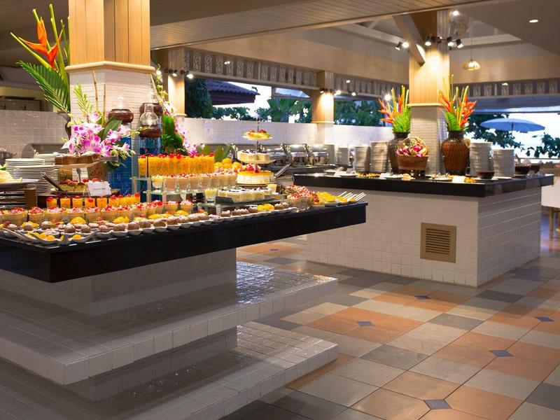 Modern buffet station with fruits, juices, and flowers in a hotel restaurant.