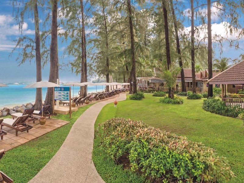 Green garden path leads to beach chairs by turquoise sea under blue sky.