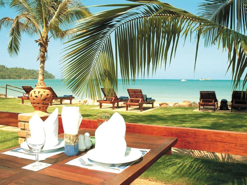 Table set with drinks overlooking a tropical beach scene with palm trees and lounge chairs.