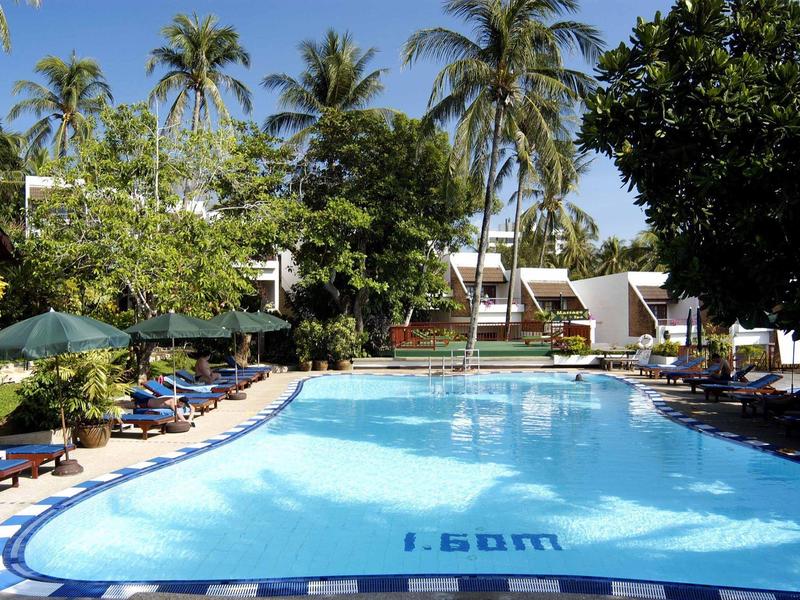 Helder zwembad in een tropische hotel tuin met palmbomen en ligstoelen aan de rand.