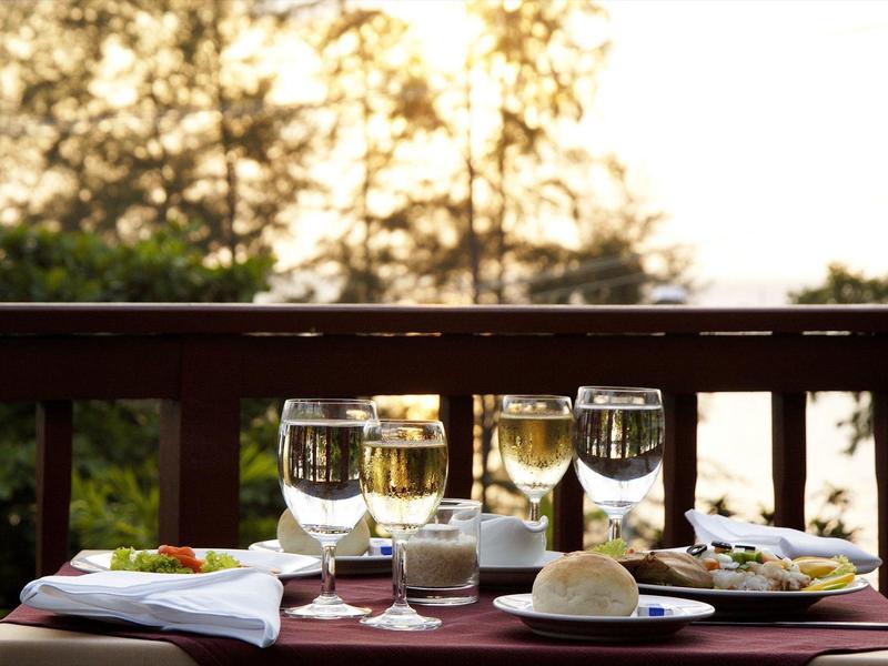 Vier wijnglazen, brood en borden met eten op een houten buitentafel bij zonsondergang.