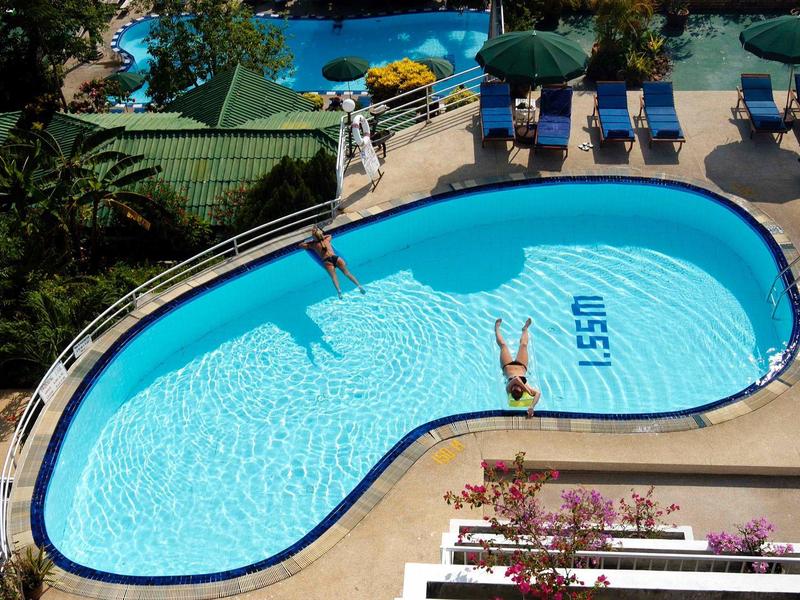 Hotelzwembad met twee personen, ligstoelen en parasols buiten.