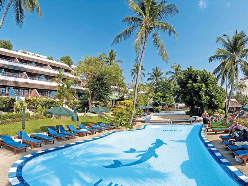 Groot buitenzwembad met ligstoelen en palmbomen voor een hotelgebouw bij een heldere lucht.
