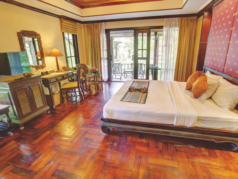 Gemütliches Hotelzimmer mit großem Bett, Holzfußboden, Schreibtisch und Balkon mit Gartenblick.