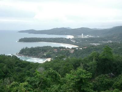 Küstenlandschaft mit bewaldeten Hügeln und breiten Sandstränden unter bewölktem Himmel.