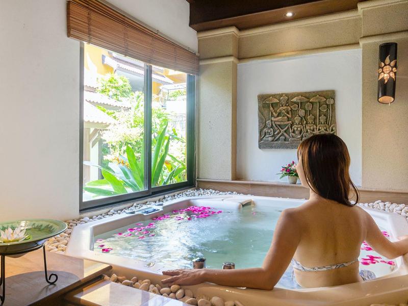 Frau im Wellnessbereich entspannt im Whirlpool, helle Räume, große Fenster mit Blick auf grüne Pflanzen.