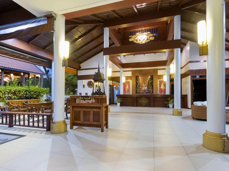 Großer, heller Empfangsbereich mit weißem Boden, Holzmöbeln und hohen Säulen in warmem Licht.