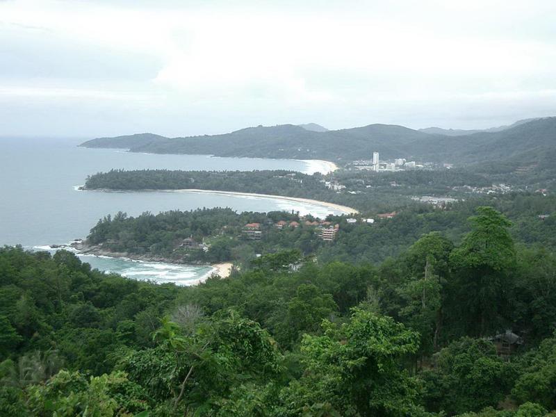 Küstenlandschaft mit bewaldeten Hügeln und breiten Sandstränden unter bewölktem Himmel.