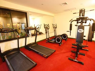 Fitnessraum mit Laufbändern, Heimtrainern und einem Mehrzweck-Kraftgerät auf rotem Teppichboden.