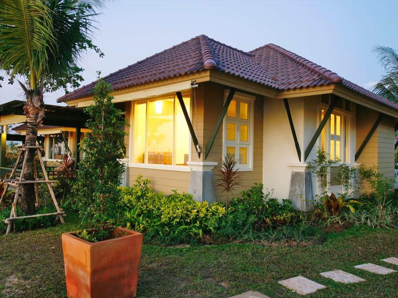 Ein kleines, hell erleuchtetes Haus mit roten Ziegeln, umgeben von Palmen und grünem Garten.