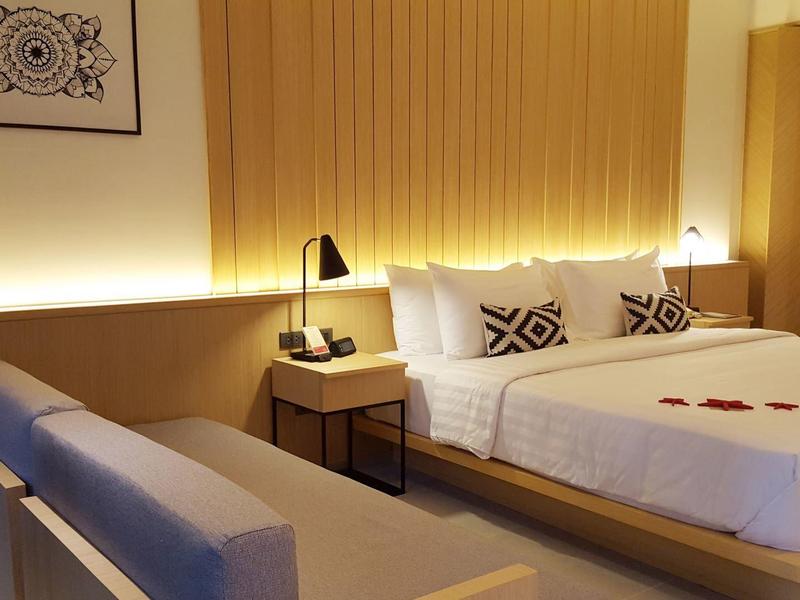 Modern eingerichtetes Schlafzimmer mit großem Bett, grauem Sofa und warmem Licht.