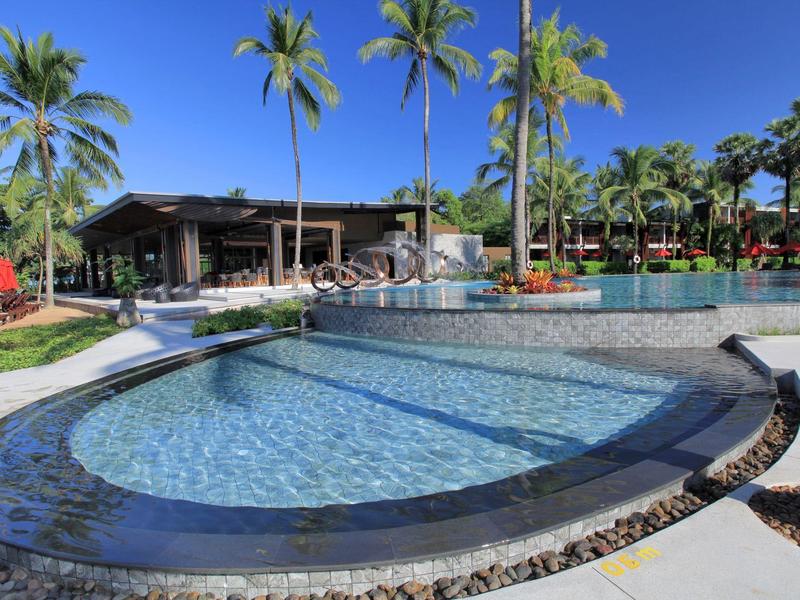 Rundlicher Pool mit klarem Wasser, umgeben von Palmen und einem Gebäude im Hintergrund.