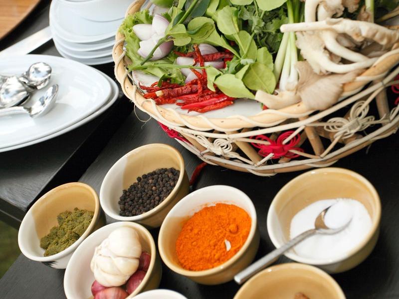 Verschiedene Gewürze und frische Kräuter in Schälchen und einem Korb auf einem Holztisch.