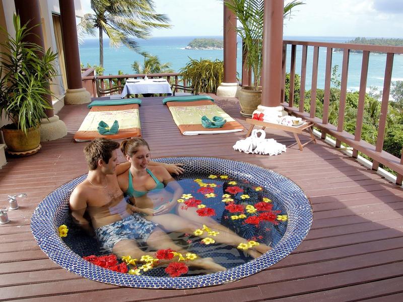 Koppel ontspant in een met bloemen gevulde dompelbad op een houten terras met uitzicht op zee.