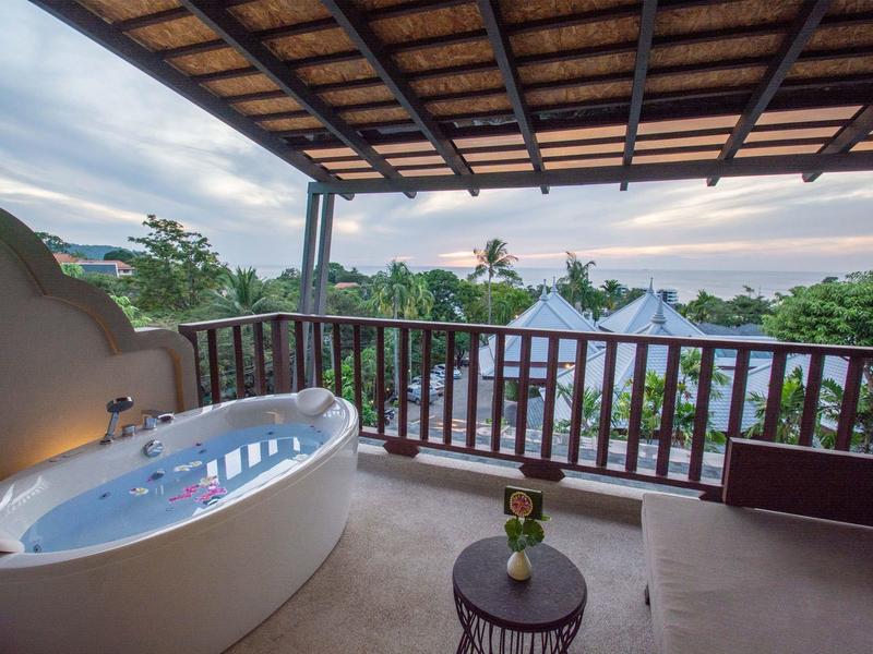 Balkon met bubbelbad, bank en uitzicht op tropische tuin en lucht.