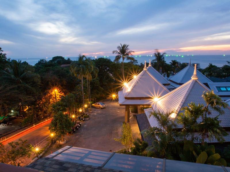 Uitzicht op een tropisch hotelresort bij zonsondergang met verlichte paden en de zee op de achtergrond.