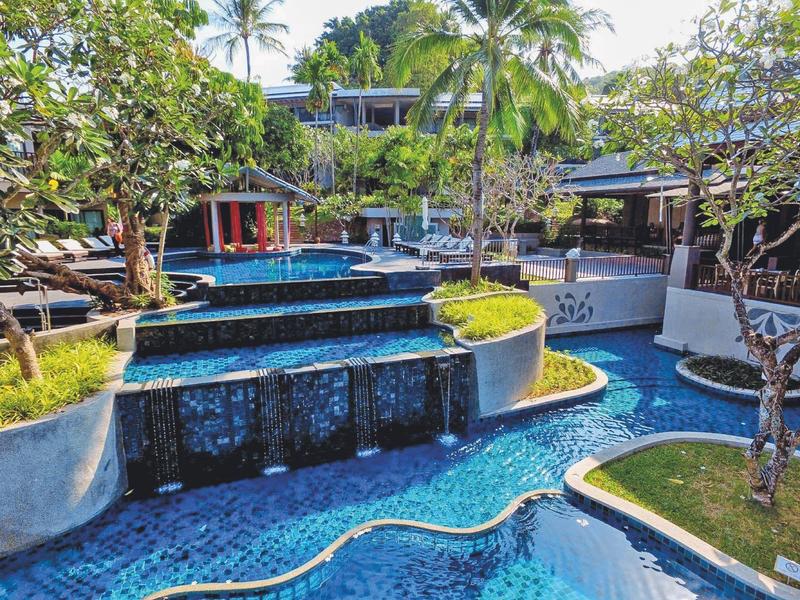 Hotelzwembad met waterval en palmbomen in een tropische vakantiesfeer.
