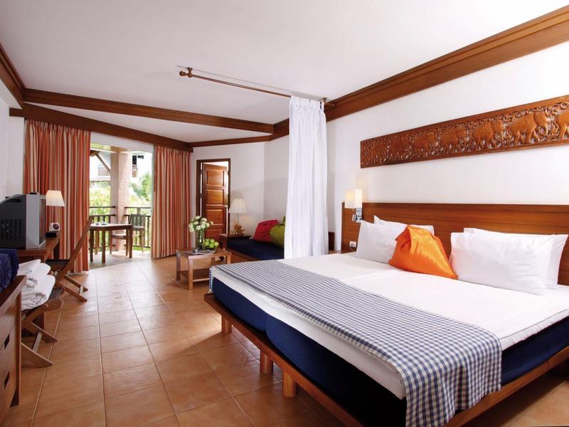 Helles Hotelzimmer mit Doppelbett, Holzmöbeln und Balkon mit Blick ins Grüne.