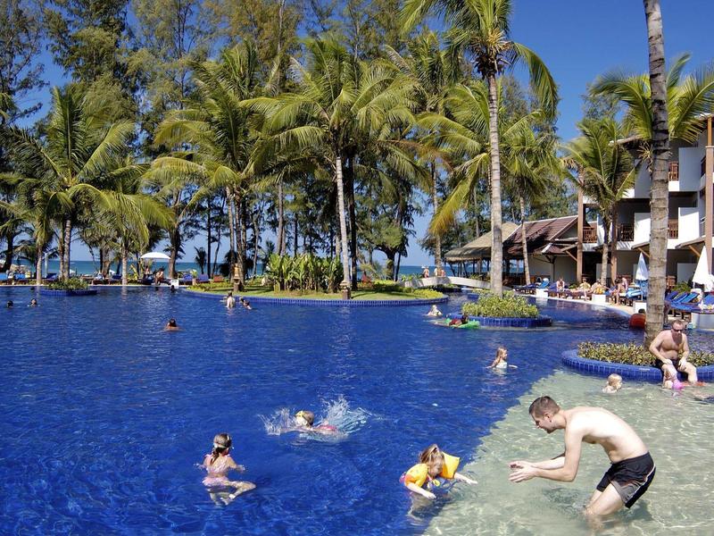 Belebter Pool mit Menschen und Palmen in tropischem Resort unter klarem Himmel.