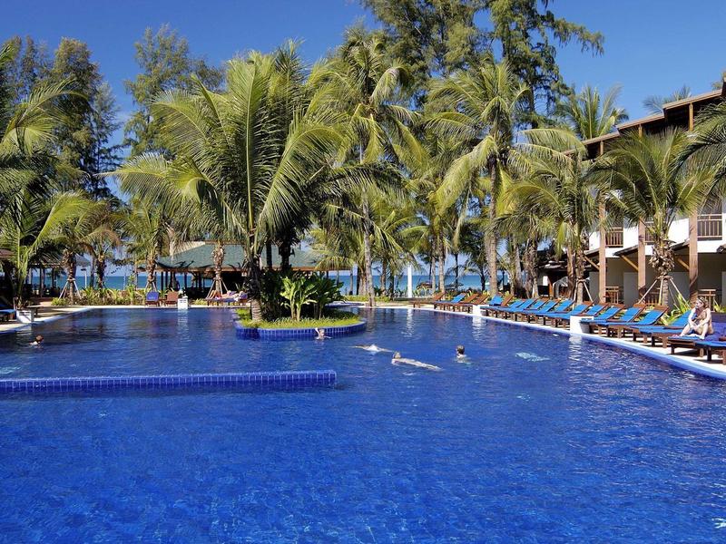 Großer Außenpool in tropischer Hotelanlage mit Palmen und Liegestühlen.