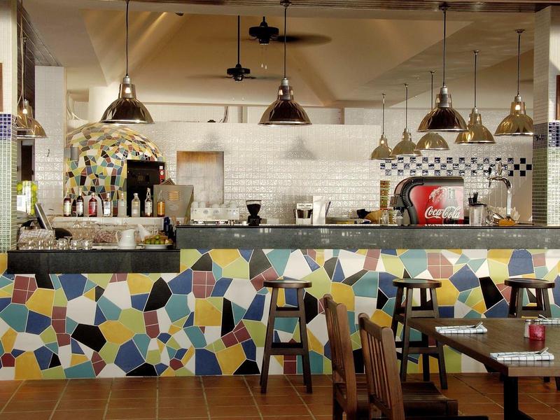 Moderne Hotelbar mit bunten Mosaikfliesen und hängenden Lampen über dem Tresen.