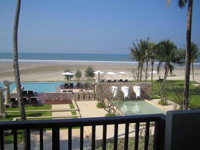 Strand mit blauem Meer, Palmen, Schwimmbad und Liegestühlen bei klarem Himmel.