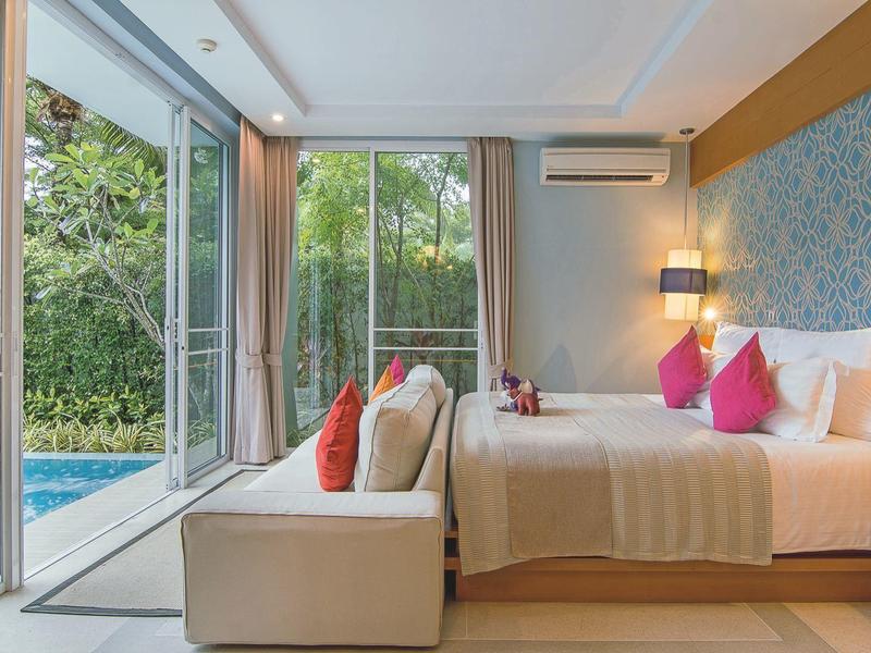 Helles Schlafzimmer mit großem Fenster, Doppelbett, bunten Kissen und Blick auf den Pool und Garten.