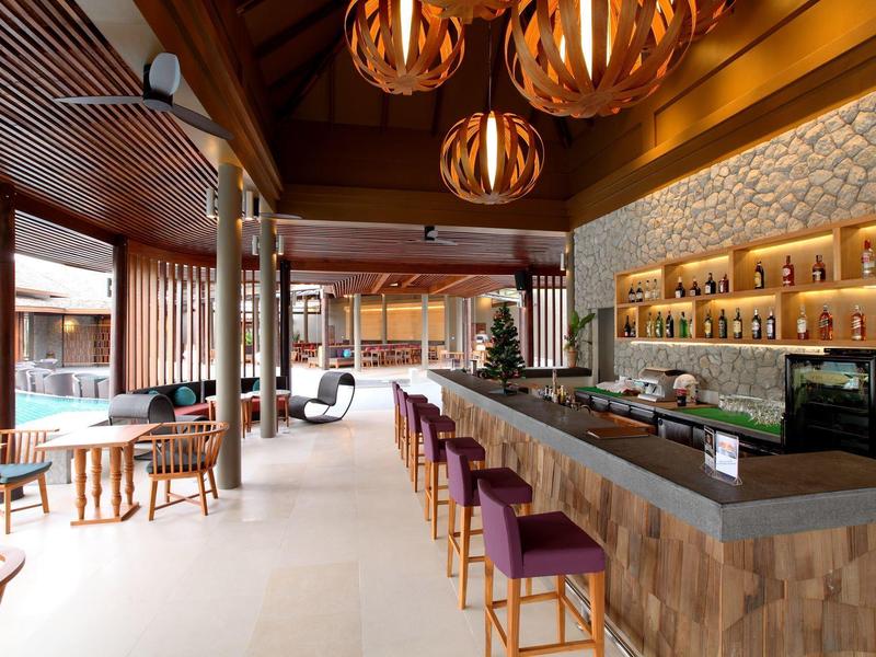 Modernes Restaurant mit langem Holzbar, lila Hockern, hängenden Lampen und hellen Böden.